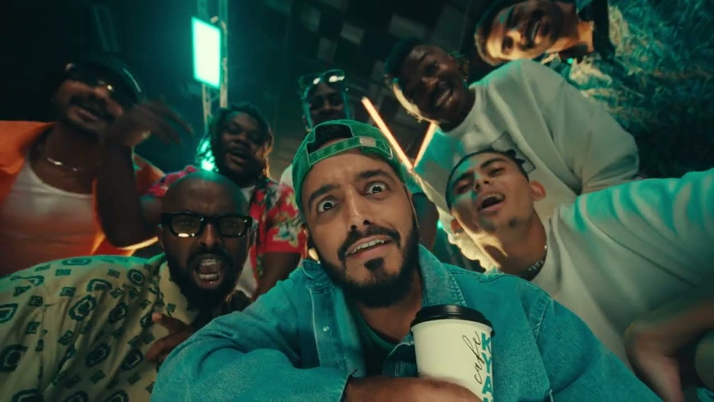 Tareq Al-Harbi and a group lean toward the camera under green neon light.