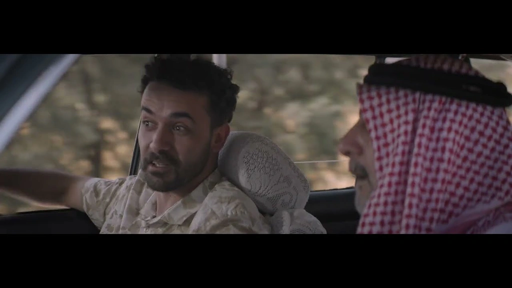 Two men in conversation inside a car in daylight.