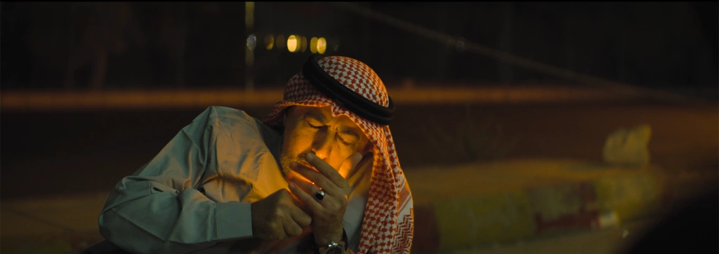 A man in a red-and-white keffiyeh lighting a cigarette, his face illuminated by the flame.