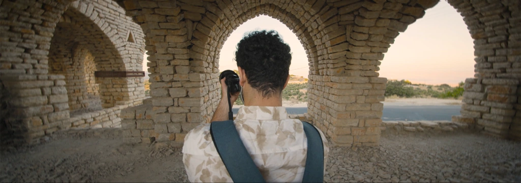 A photographer seen from behind beneath stone arches in warm evening light.