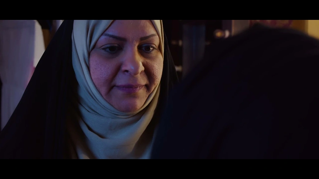 An older woman in a pale headscarf, lit with a mix of blue and warm light.
