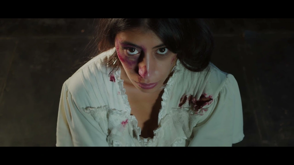 A woman with theatrical blood on her face looks toward the camera in a tense scene.