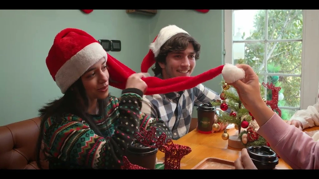 Friends sharing a red Christmas scarf around a café table.