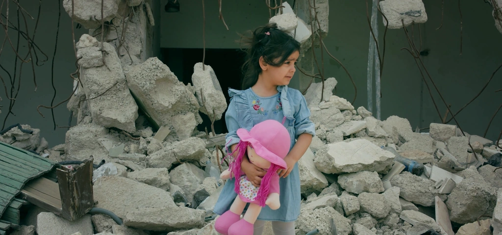 A girl with a pink toy stands among pale concrete rubble.