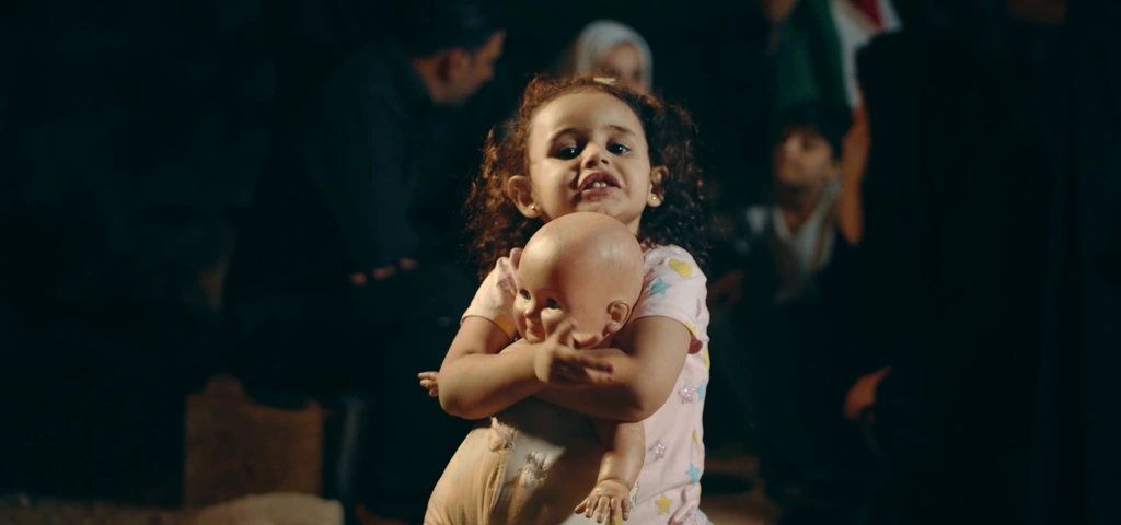 A child holds a doll in the warmly lit interior sequence.