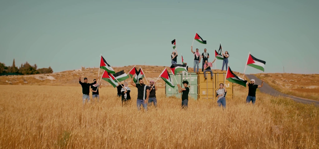 A wide view of the performers and Palestinian flags across a golden field.