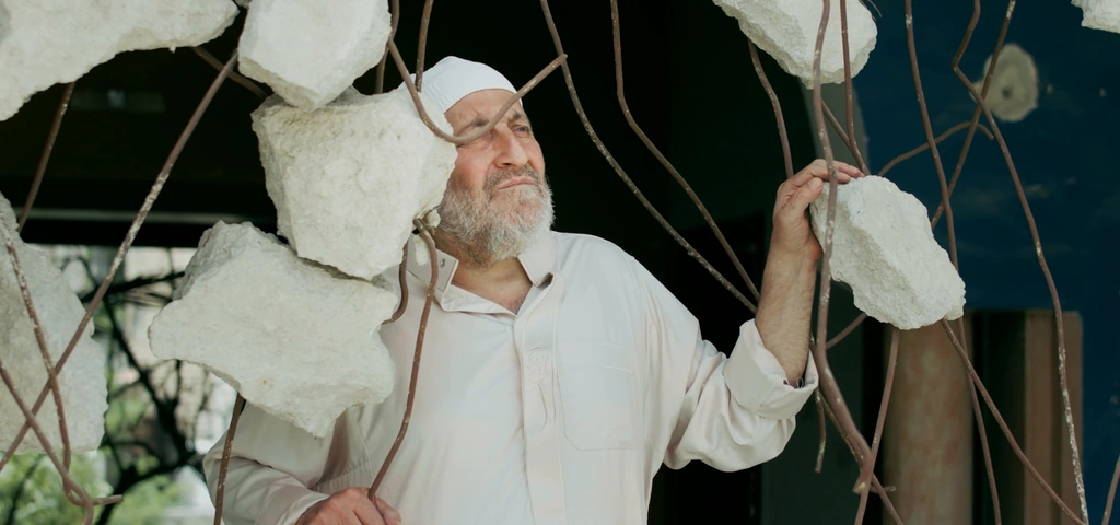 A close portrait of an older man framed by broken concrete and exposed metal.