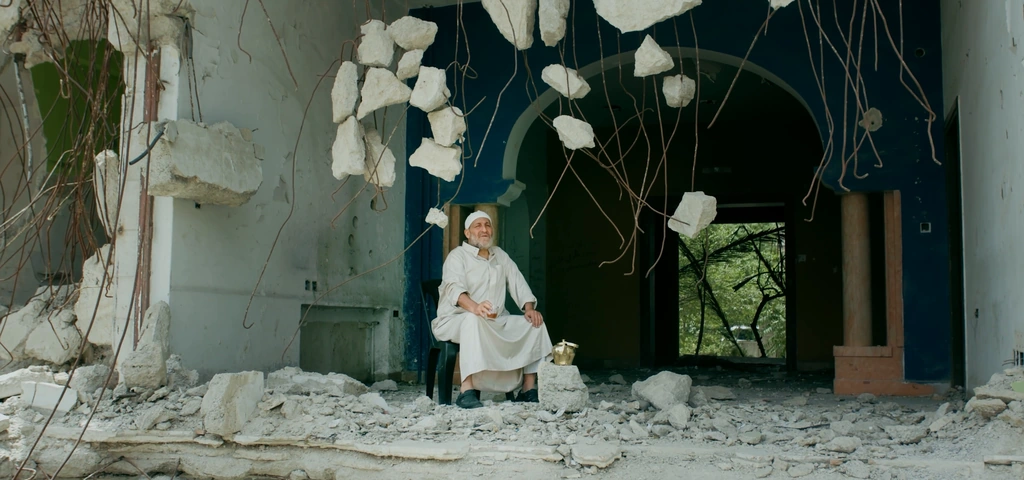 An older man sits amid the open walls and rubble of a building set.