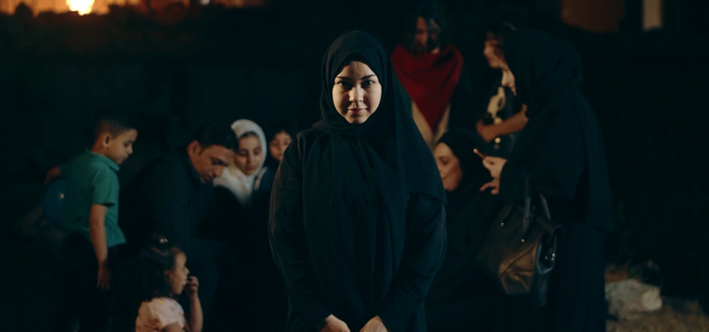 A woman stands in the foreground of a warmly lit group scene.