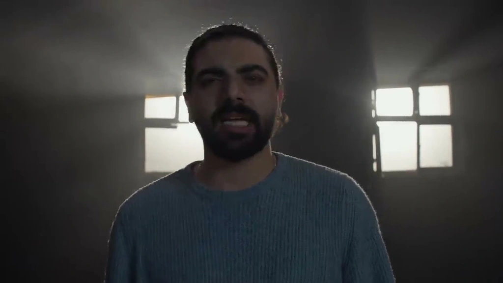 Alawar in a blue sweater, with bright windows behind him.