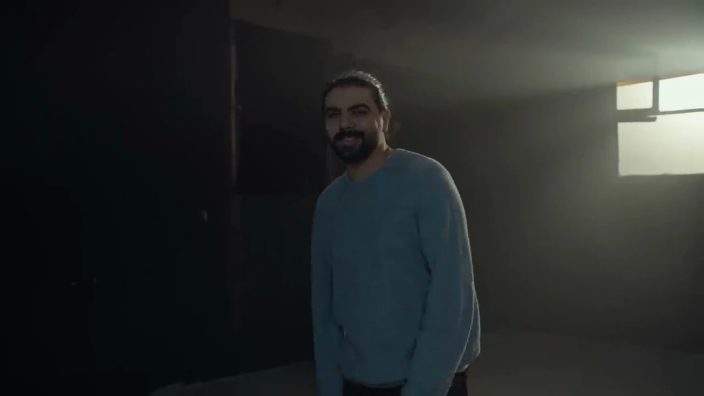 Alawar standing in a dark room crossed by shafts of window light.