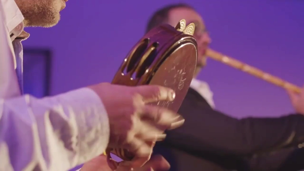 A frame drum fills the foreground, with the woodwind player softly behind.