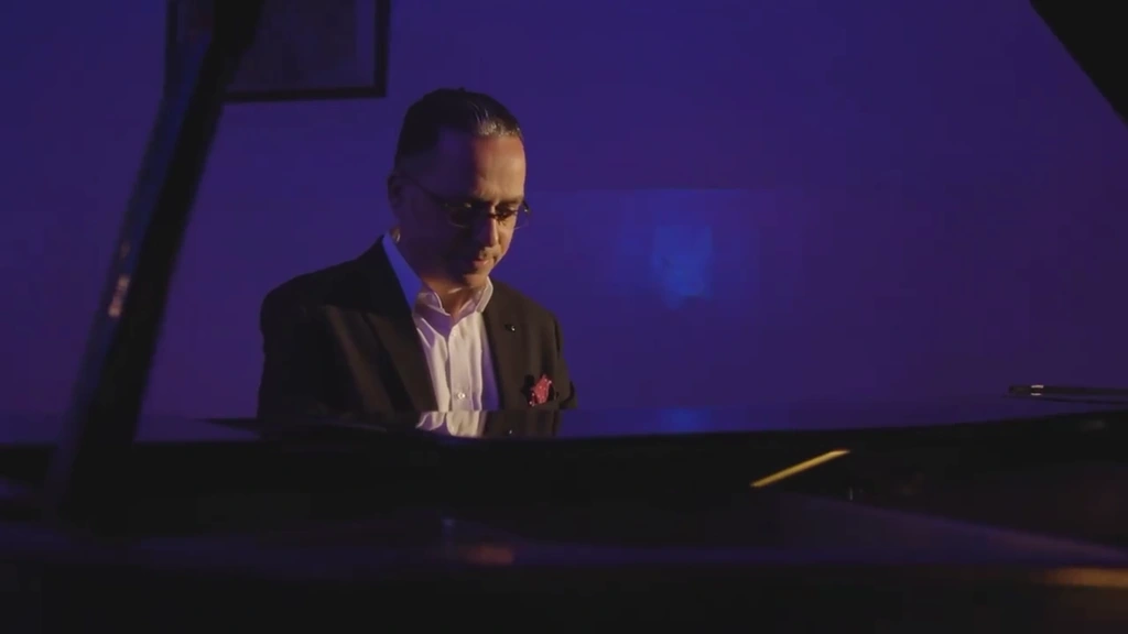 A pianist in a dark jacket and white shirt framed above the grand piano.