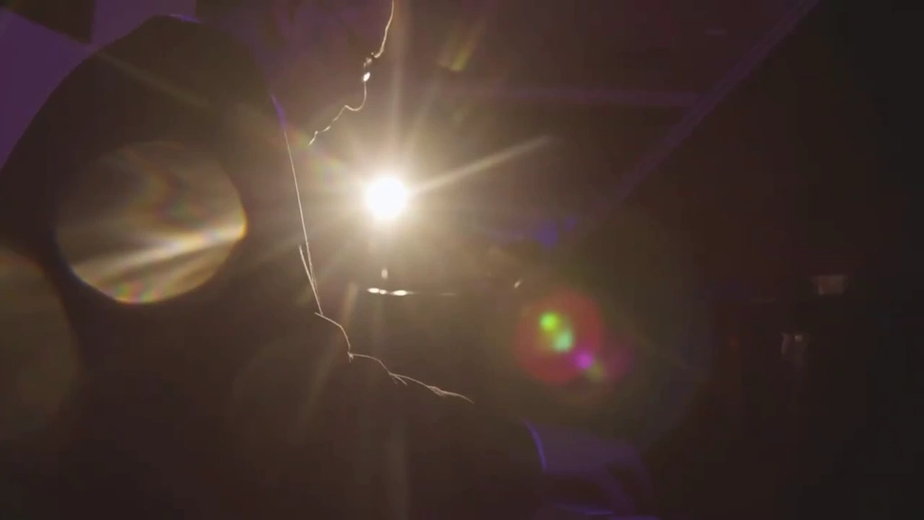 The woodwind player is silhouetted against a bright stage light and lens flare.