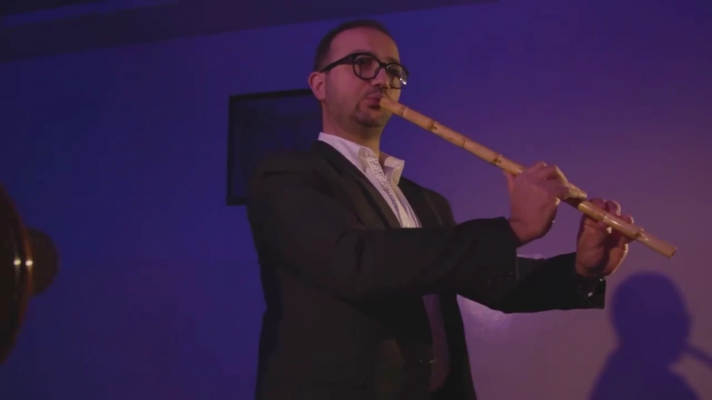 A musician plays a wooden flute against a softly lit violet wall.