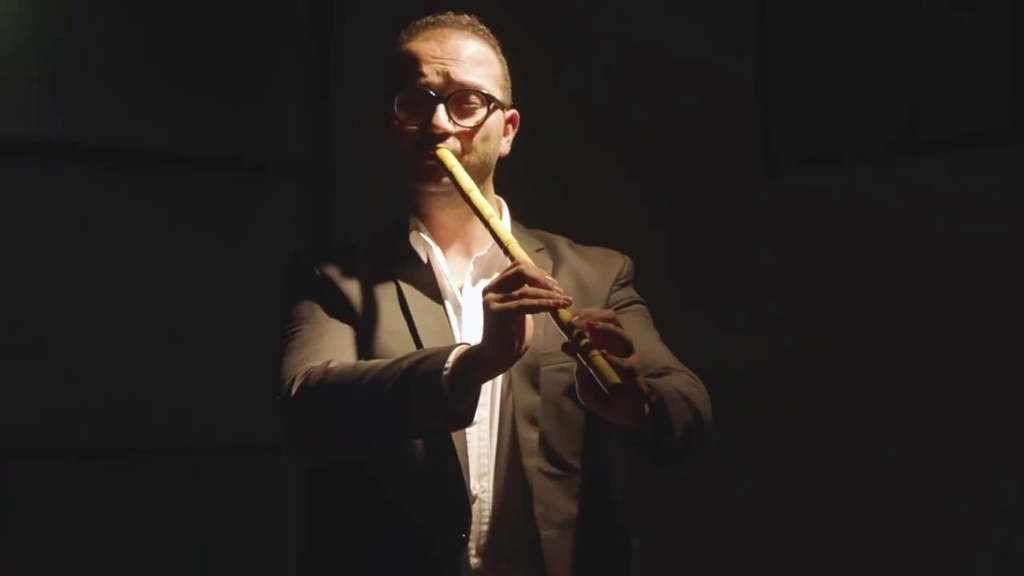 A woodwind player is isolated against darkness by warm stage light.