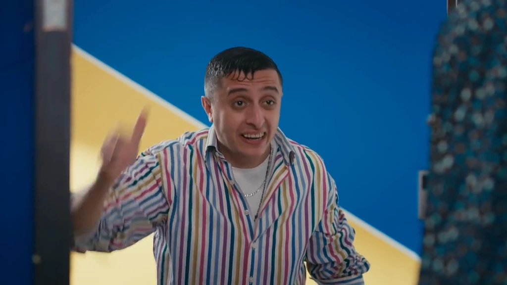 A smiling character in a striped shirt against an angular blue-and-yellow wall.