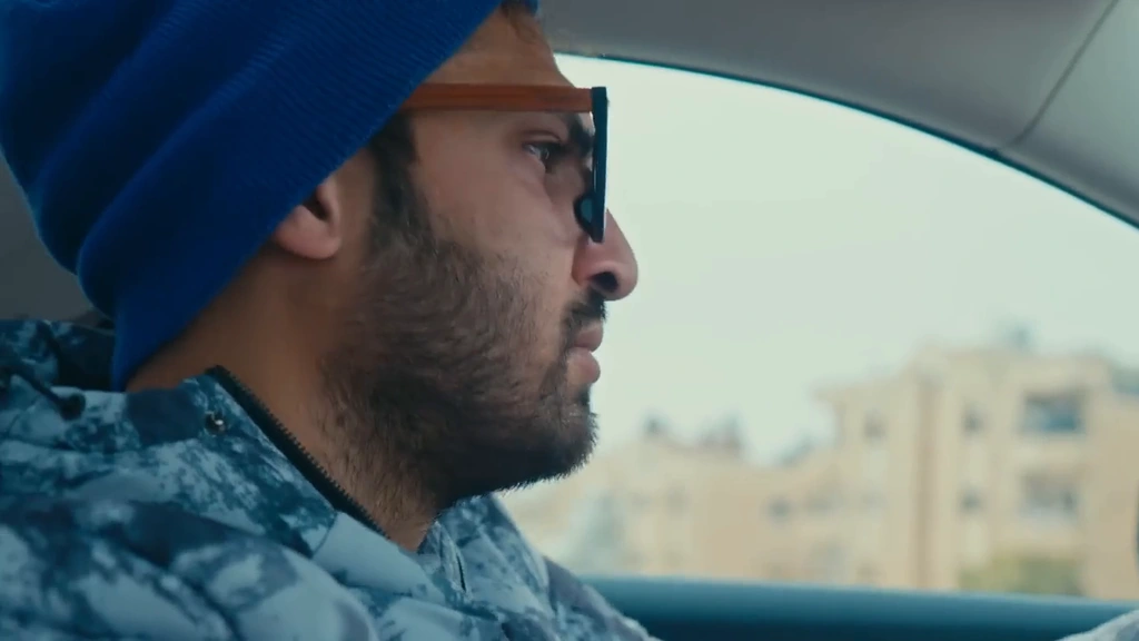 A driver in a blue cap seen in profile inside a car in daylight.