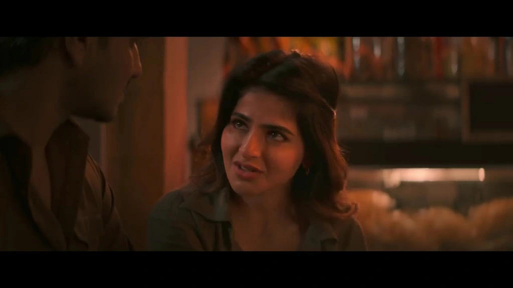 A woman in conversation across a table in a warm-lit interior.