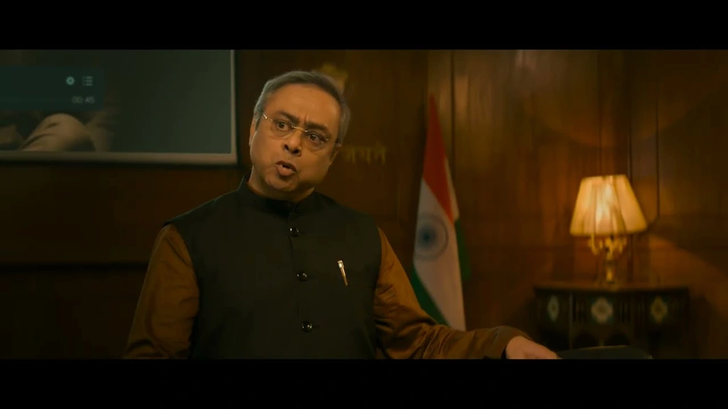 SPY — Warm office interior with a man seated beside an Indian flag.
