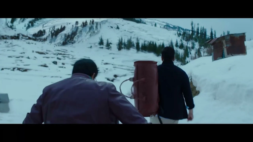 SPY — Two men and a large pack moving through a snowy landscape.