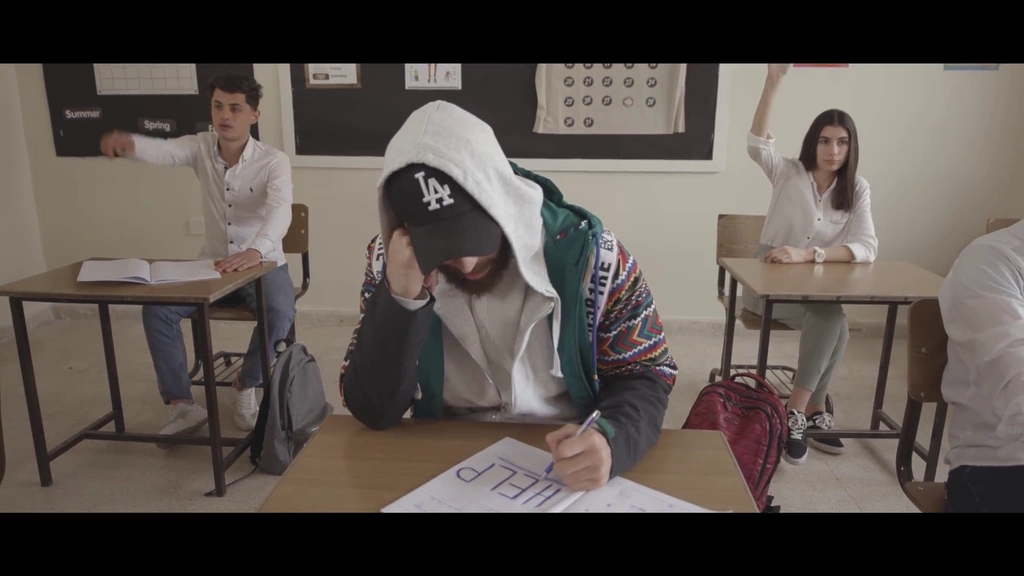 llunr sits in the foreground of a classroom while students sit behind him.