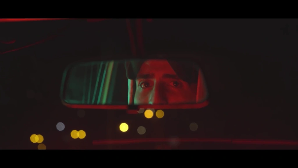 llunr’s eyes reflect in a car mirror amid red light and distant bokeh.