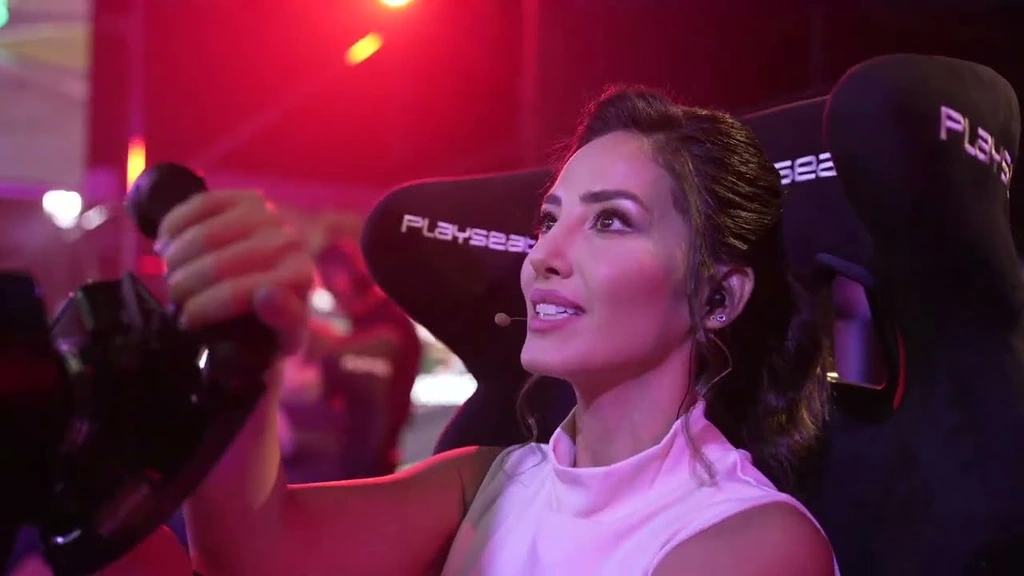 A woman at a racing simulator under magenta event lighting in the Toyota event broadcast.