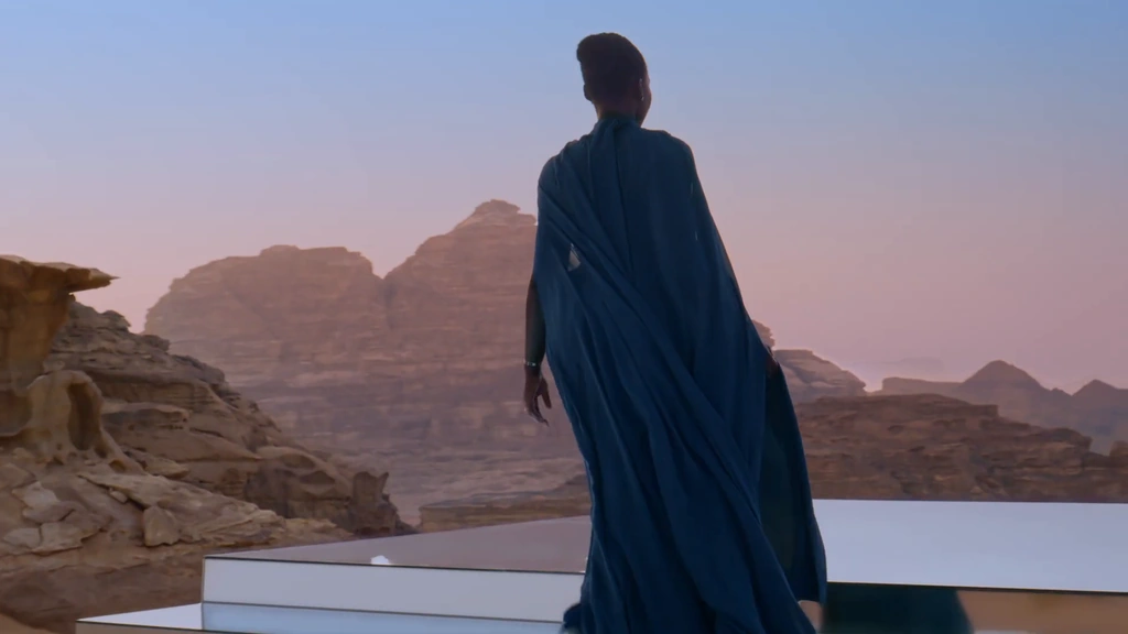Lupita Nyong’o in a flowing blue dress on a mirrored platform overlooking Wadi Rum at dusk.