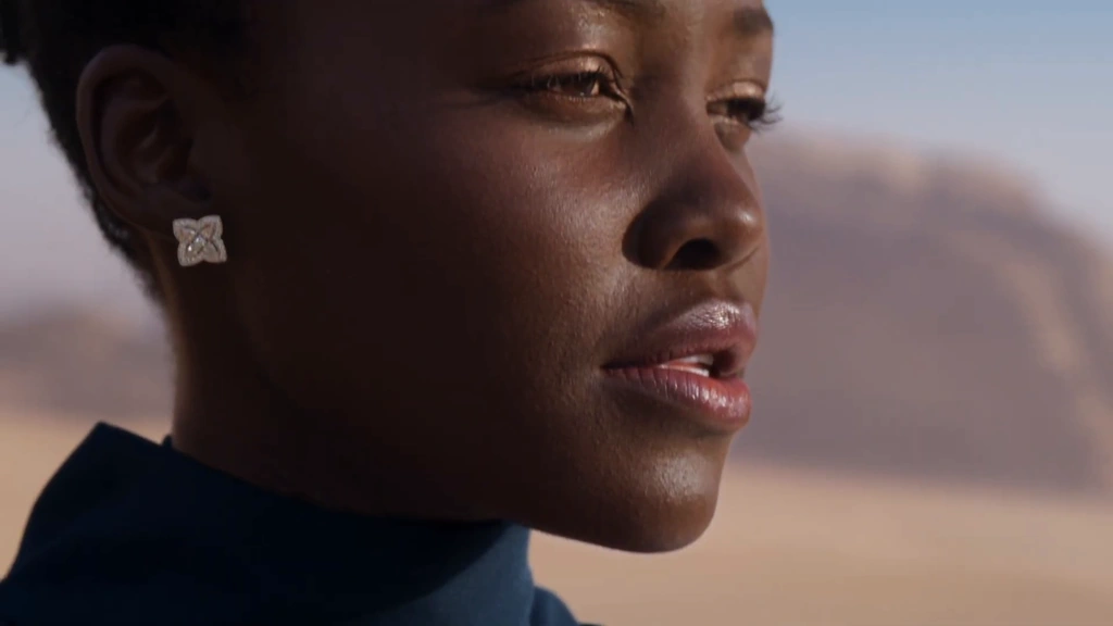 A close profile of Lupita Nyong’o with a diamond earring and softly focused sandstone beyond.
