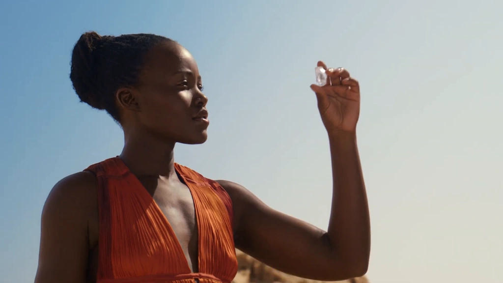 Lupita Nyong’o holds a rough diamond to the light beneath a clear blue sky.