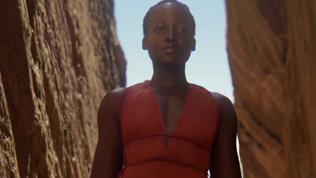 Lupita Nyong’o in a rust-red dress framed by a narrow sandstone canyon.