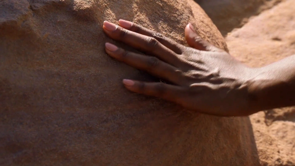 A hand rests against a sunlit sandstone wall.