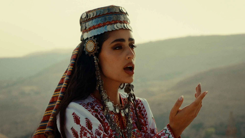 Zeyne in an embroidered outfit and headdress against sunlit hills.