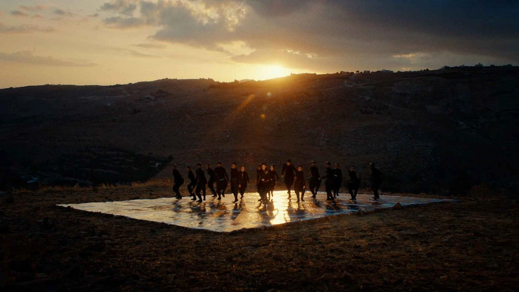 An ensemble silhouetted on a reflective platform beneath a low setting sun.